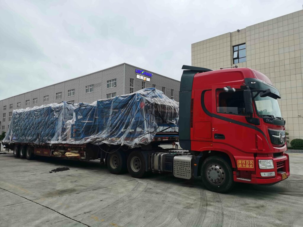 pexels-photo-29399463-29399463 Red truck with large covered cargo in an industrial area, overcast day.